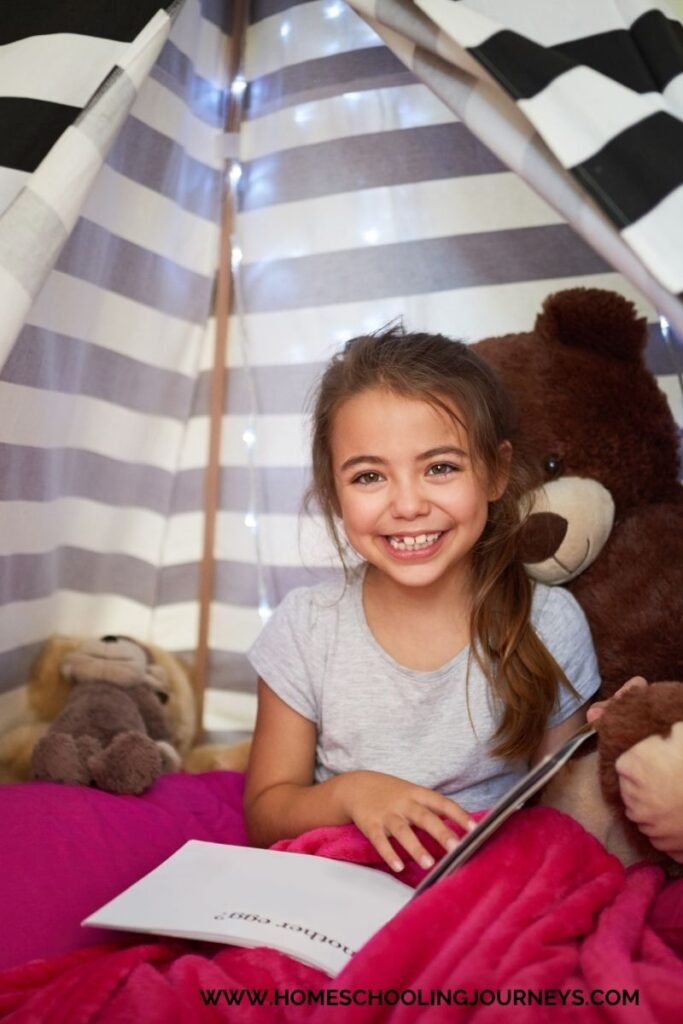 An image of a little girl in a small tent reading with a bear. 